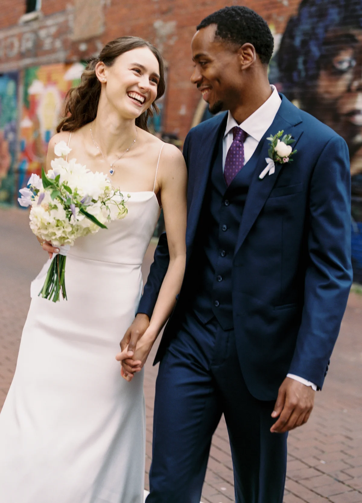 Bride holding a white and lilac wedding bouquet beside a mural on H Street, Washington DC