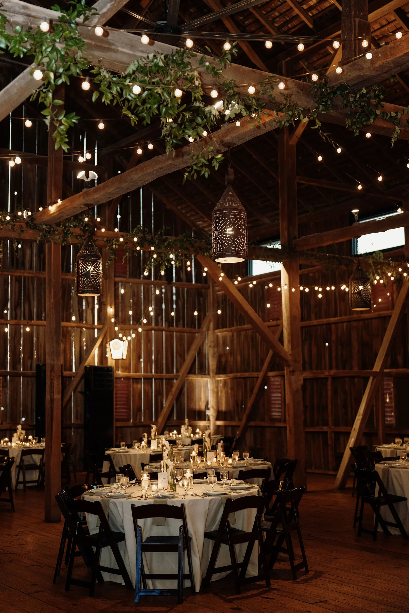 Historic bank barn wedding reception with lanterns, string lights and greenery on the beams