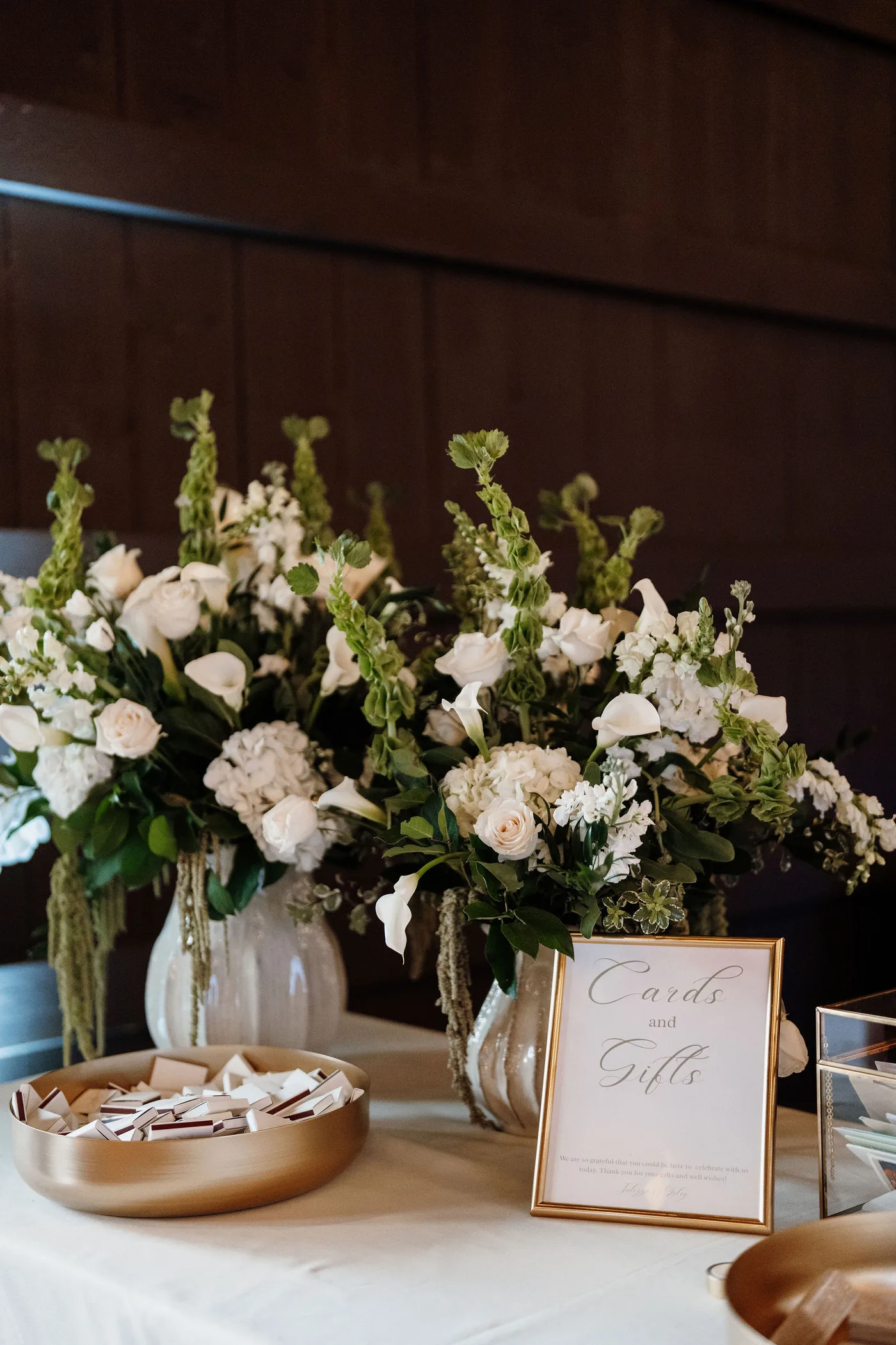Large white and green wedding arrangements on the card table at a barn reception