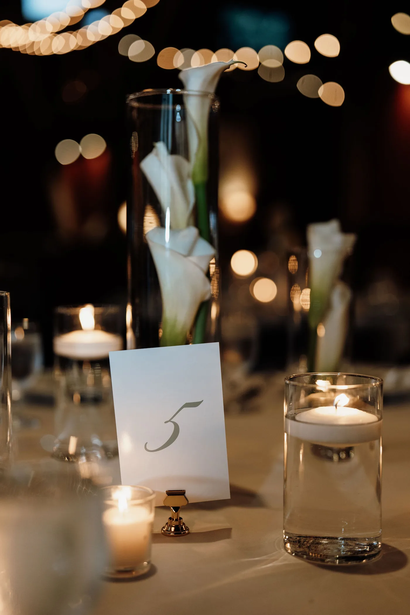 Calla lilies in glass cylinders with floating candles as a wedding centerpiece