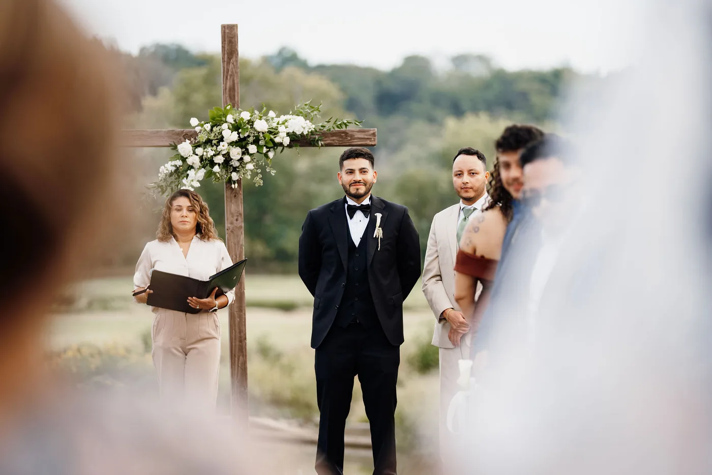 Wooden ceremony cross dressed with white flowers and greenery overlooking the water in Leesburg VA