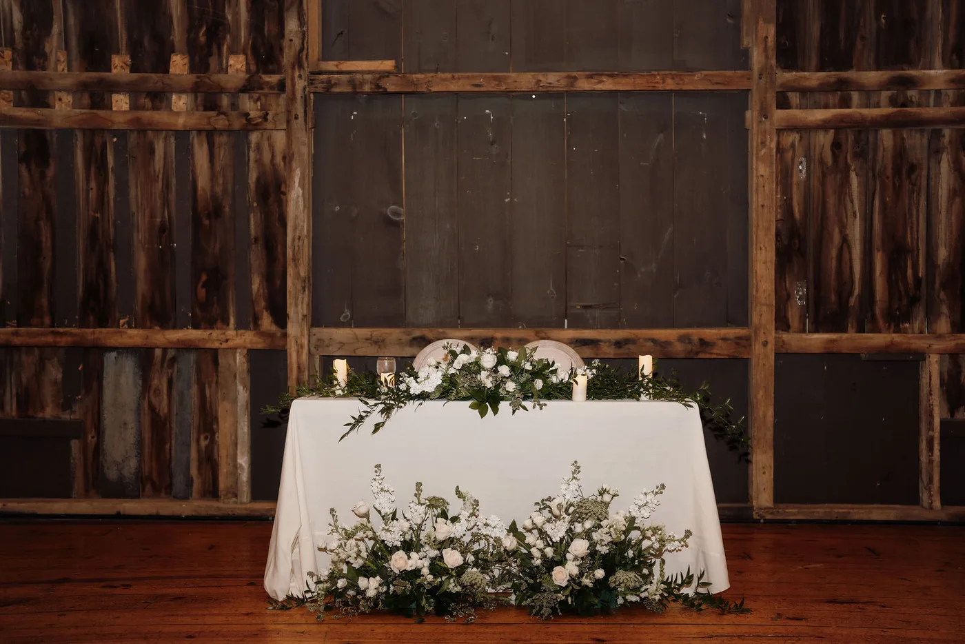 Sweetheart table with a white and green floral runner against barn boards