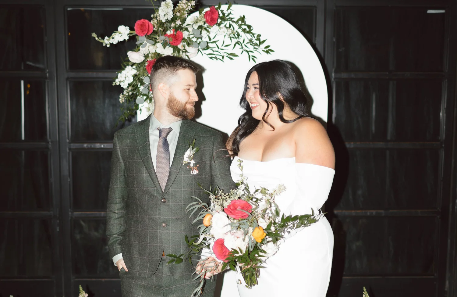Bride and groom beside a white ceremony arch dressed in crimson roses and greenery at Maketto in Washington DC