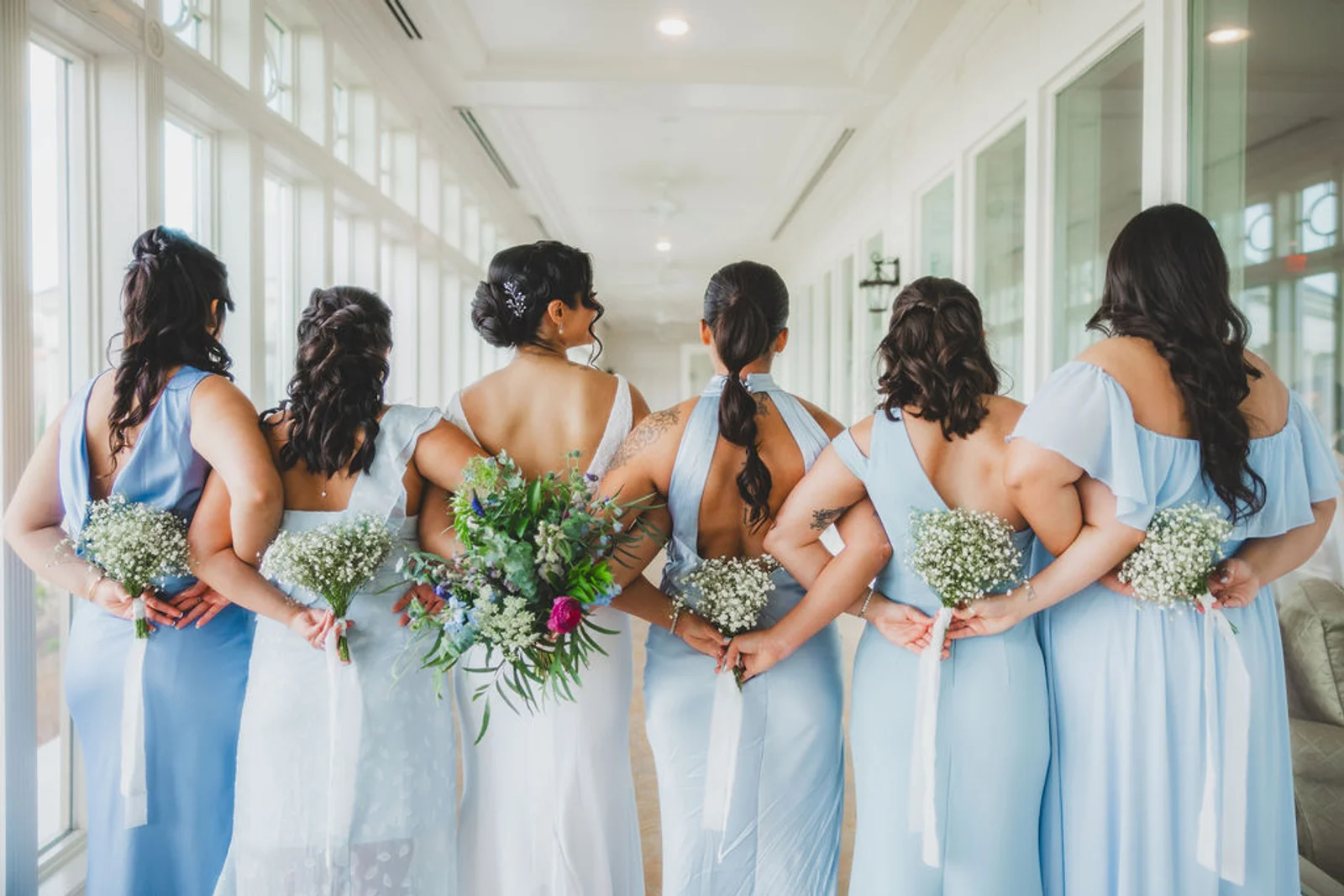 Bride and bridesmaids in pale blue holding spring bouquets behind their backs at Washington Golf & Country Club, Arlington VA